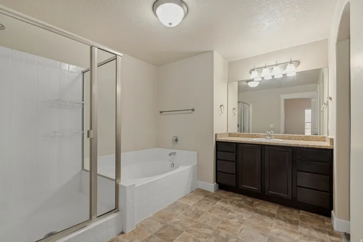 Full shower enclosure with glass door, separate soaking tub, vanity with stone countertop, large mirror, and tiled flooring