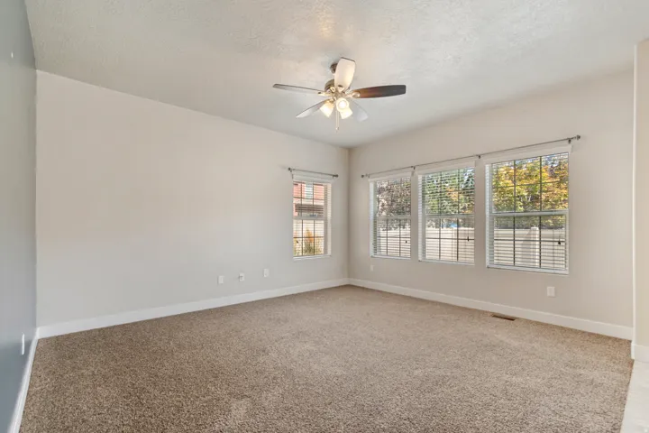 Carpeted flooring, vaulted ceiling, multi-pane windows, ceiling fan with light fixture, and vertical blinds