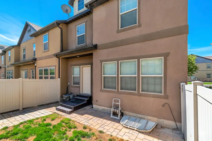 Stucco exterior with multiple windows, private fenced area, and paver patio with grass