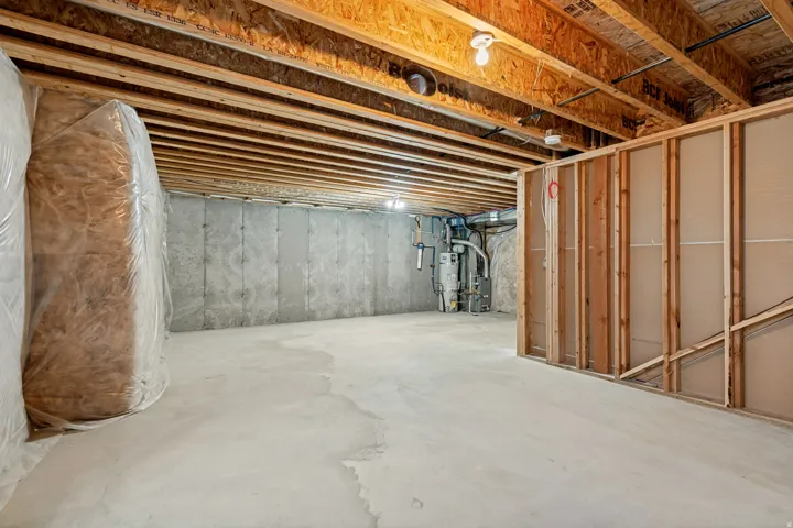 Unfinished concrete flooring, exposed wood joists, concrete foundation walls, framed wall partition, visible utility installations