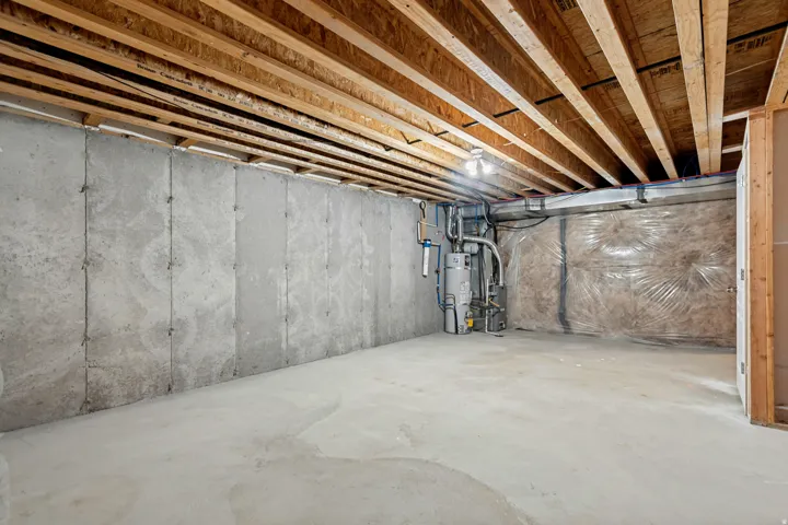 Unfinished basement with exposed ceiling joists, concrete floor, concrete walls, and visible utility connections