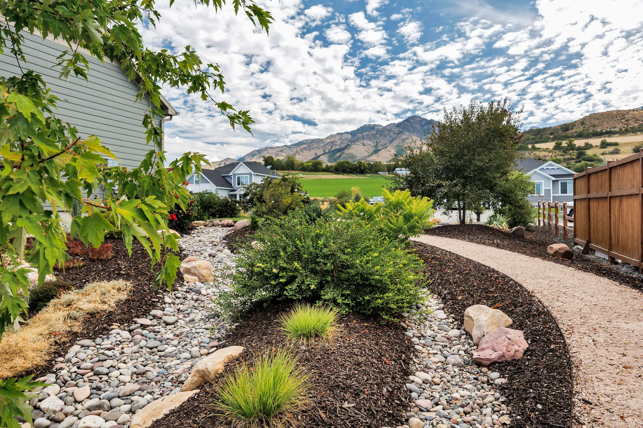 Landscaped garden path featuring decorative rock beds, a gravel walkway, and a wood fence