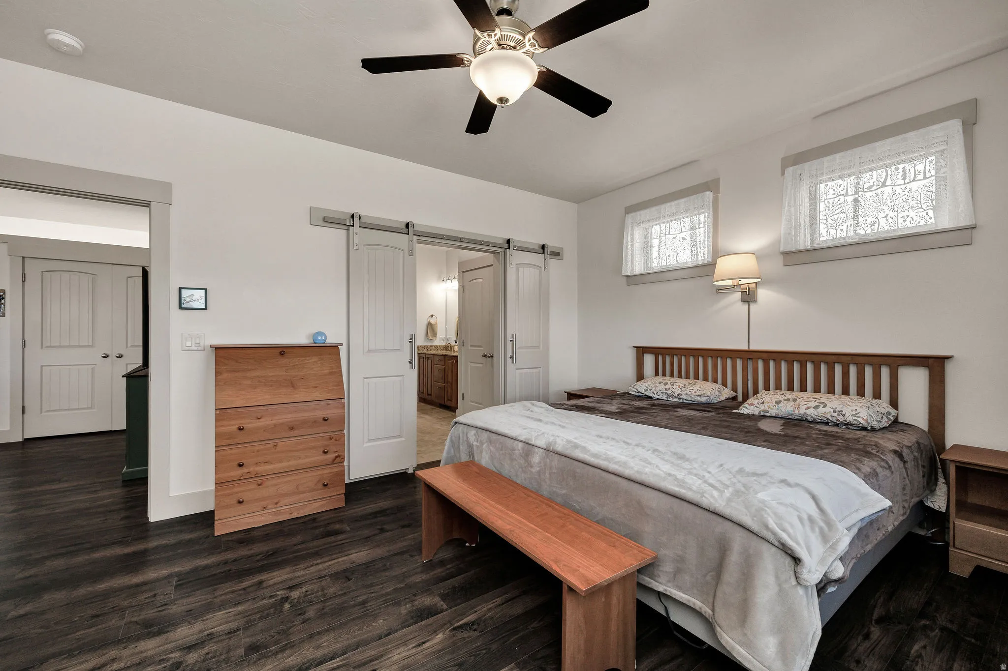 Wood-finish flooring, ceiling fan with integrated lighting, wall-mounted light fixture, dual windows, and barn door entry