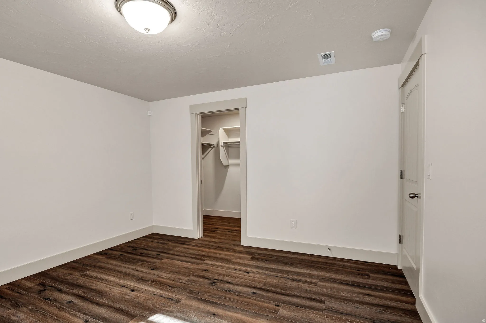 Wood-finish flooring with white baseboards, a flush-mount ceiling light, and an open closet with shelving