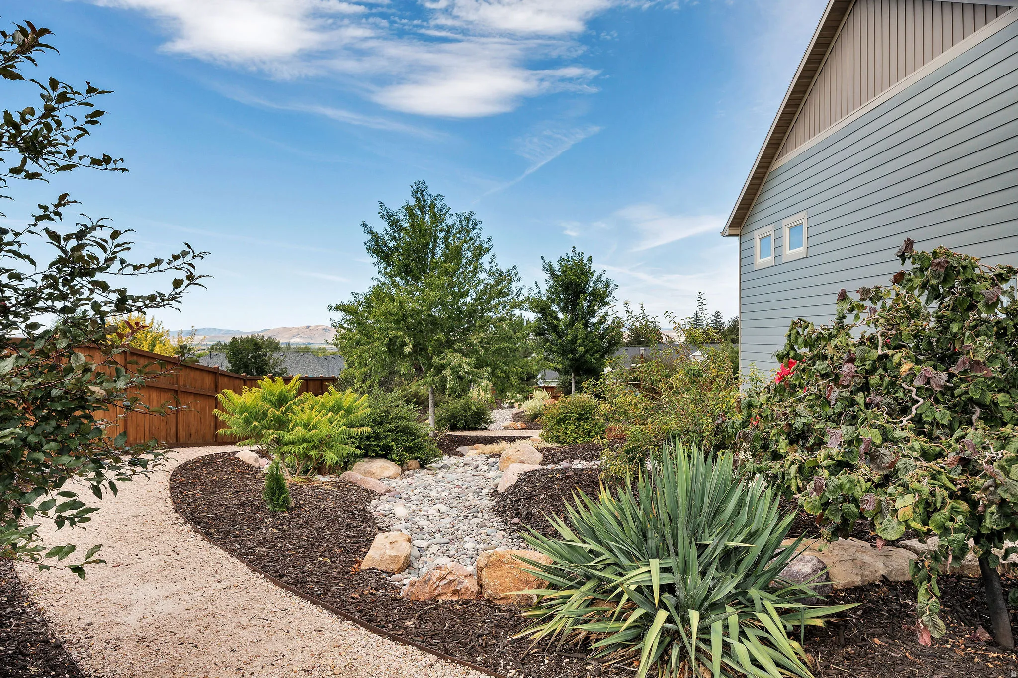 Landscaped grounds featuring a gravel pathway, wood privacy fence, and mature plantings
