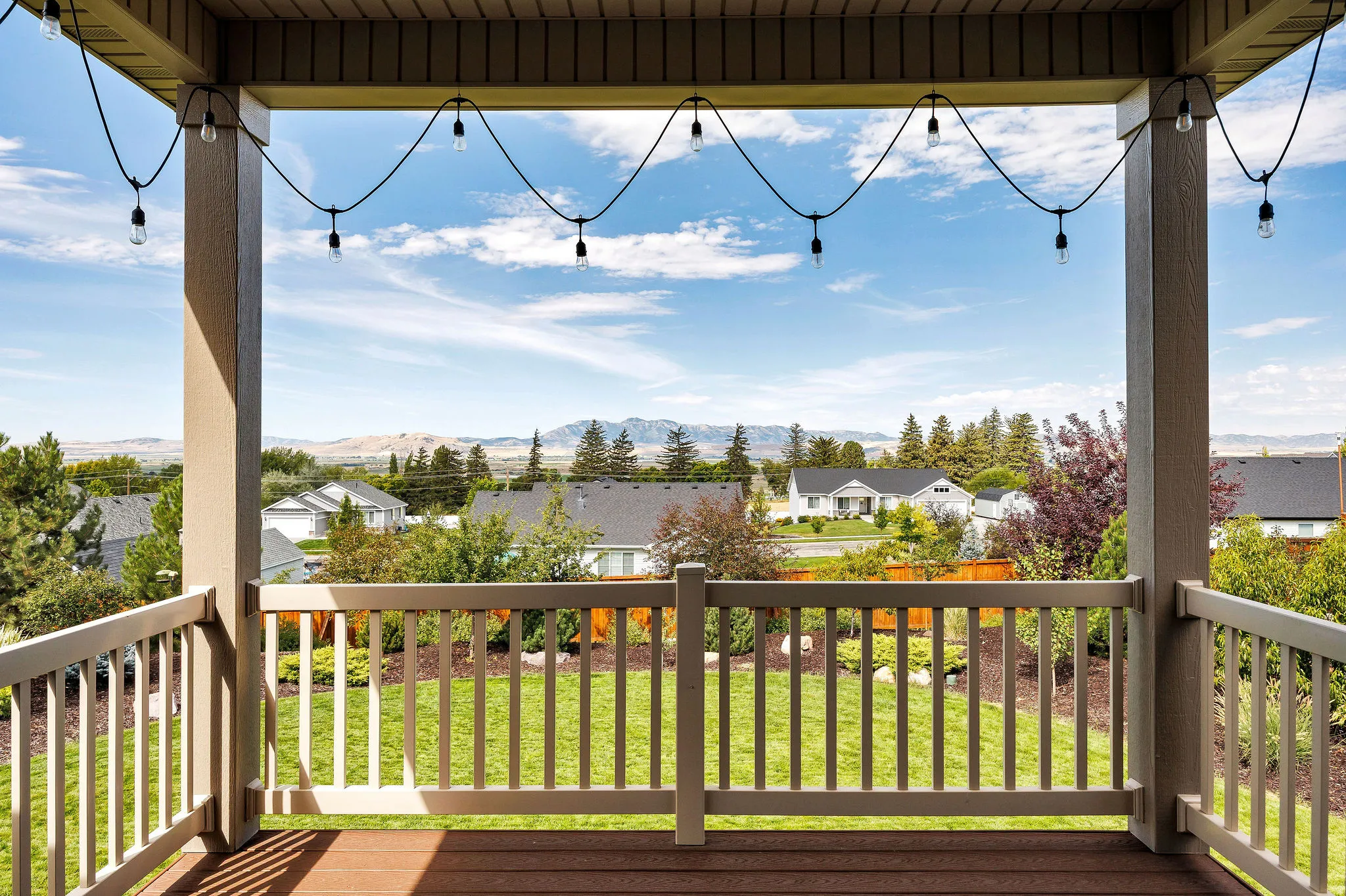 Covered exterior deck with wood-finish flooring, baluster railing, and string lighting