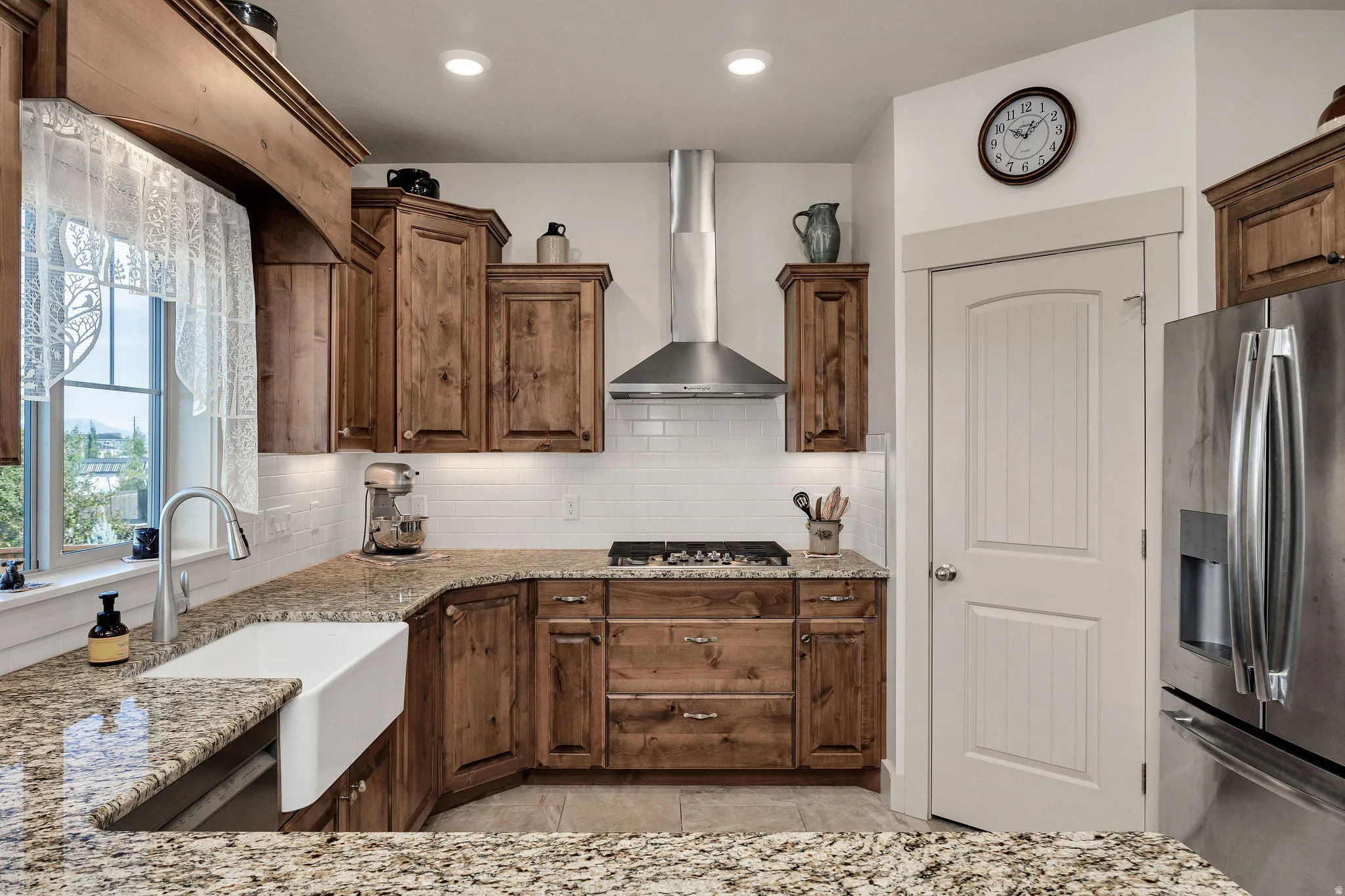 Spacious kitchen featuring wood cabinetry, granite countertops, a farmhouse sink, stainless steel appliances, and a gas cooktop with a stainless steel range hood