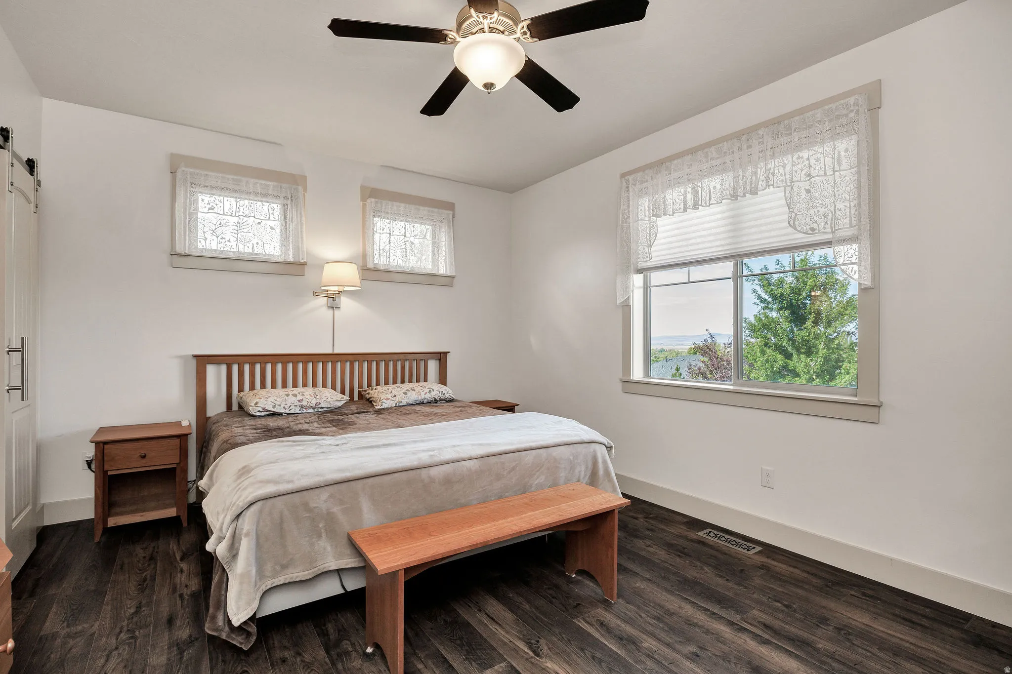 Wood-finish flooring, ceiling fan with integrated lighting, wall-mounted light fixture, and a barn door entry