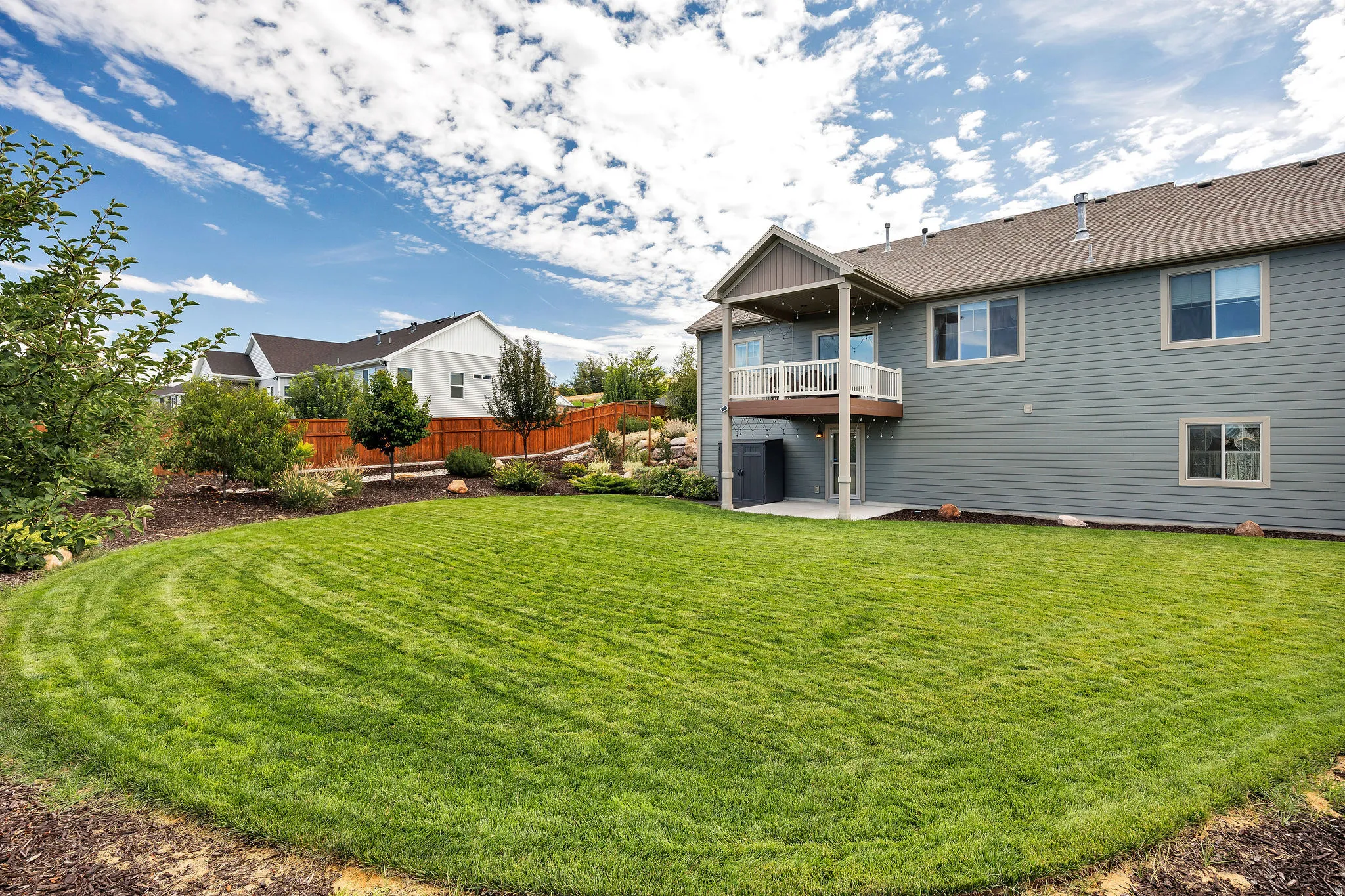 Expansive backyard with a manicured lawn, a two-story exterior with a covered deck, and an upper-level balcony