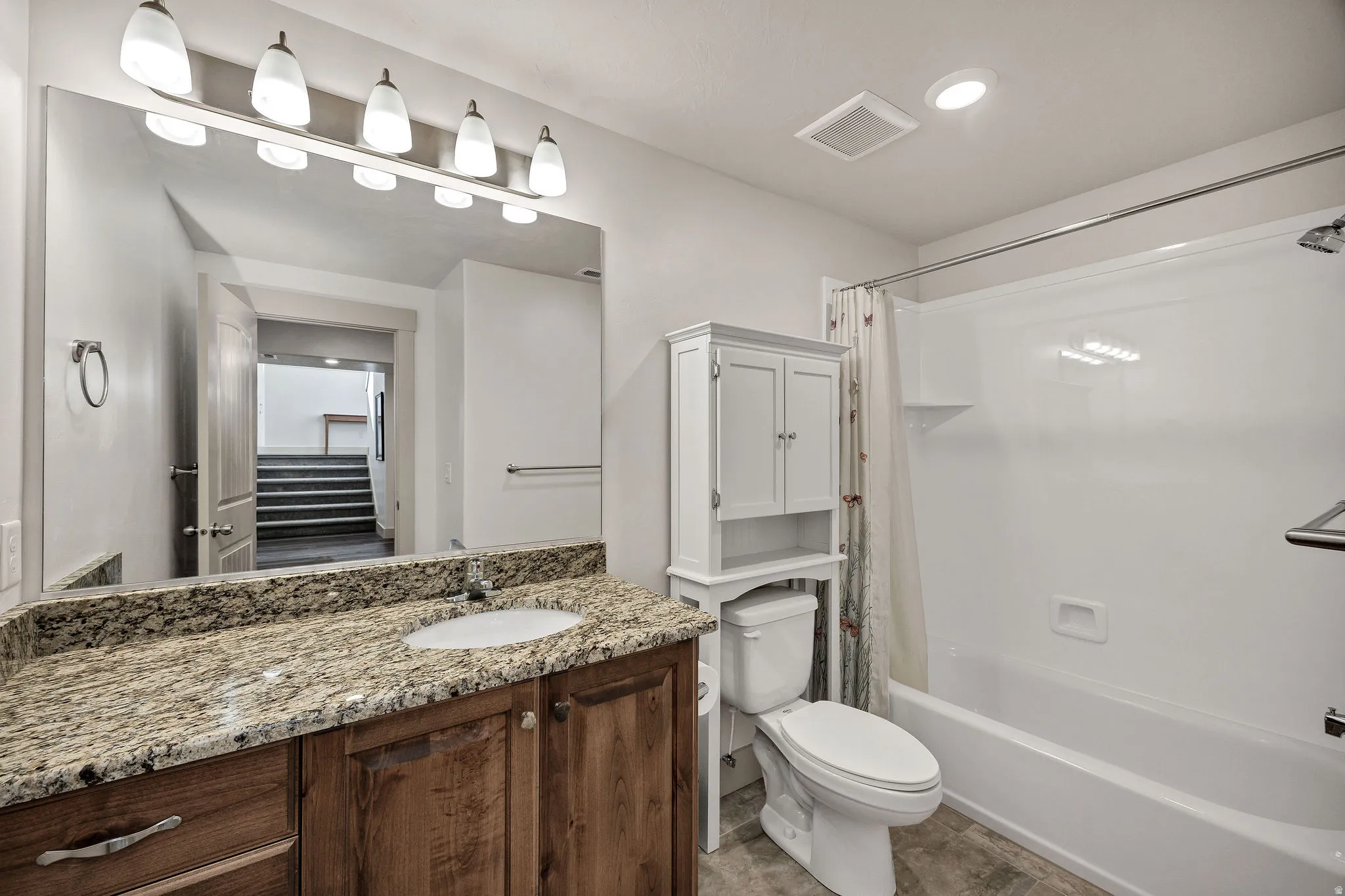 Vanity with wood-finish cabinetry, countertop with integrated sink, and large wall-mounted mirror