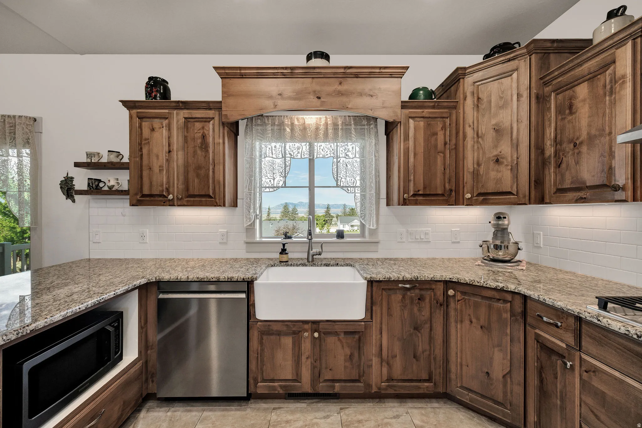 Wood-finish cabinetry with a built-in microwave, white farmhouse sink, stainless steel dishwasher, and light-toned countertop