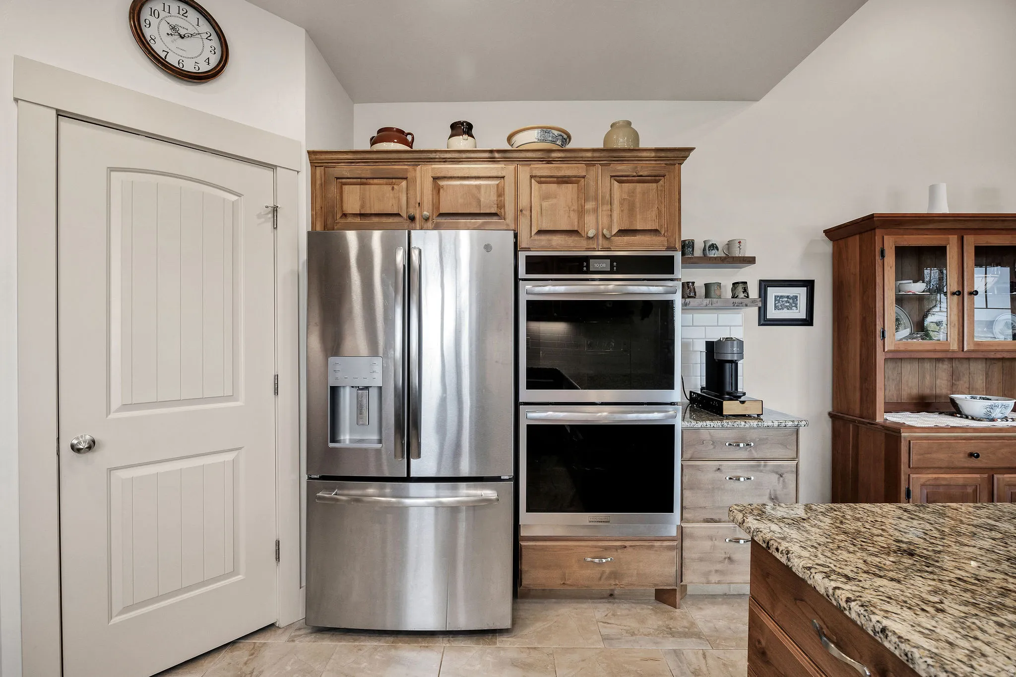 Stainless steel French door refrigerator, double wall ovens, wood-finish cabinetry, granite countertop, and subway tile backsplash