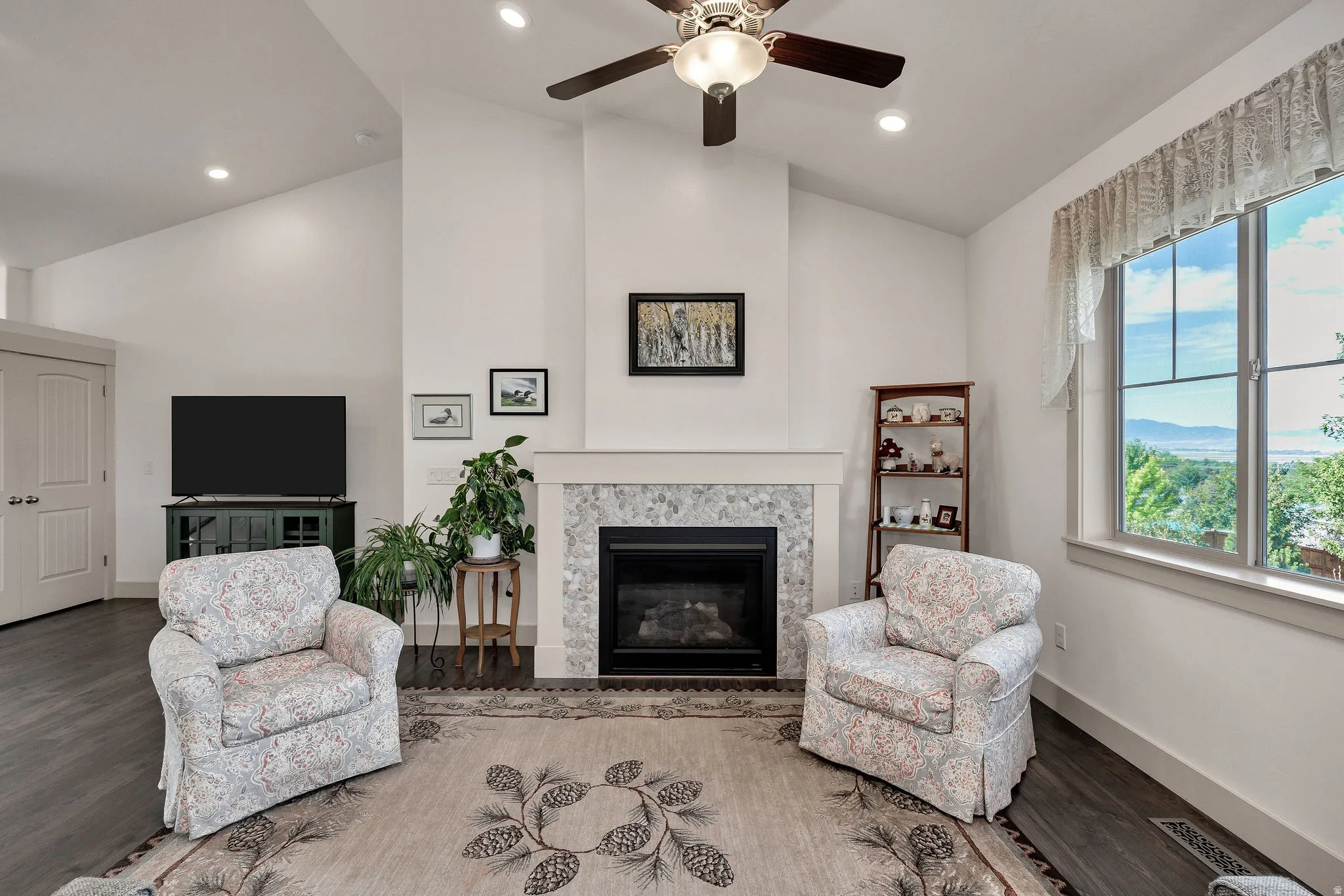 Vaulted ceiling with recessed lighting, ceiling fan, fireplace with stone surround, wood-finish flooring, and window with natural light