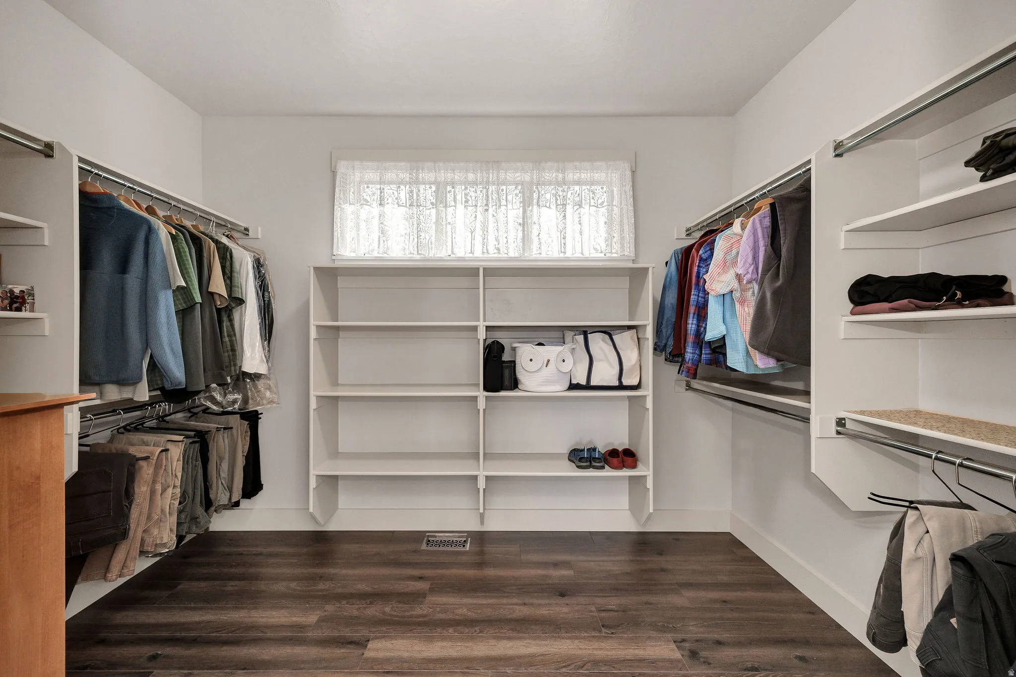Walk-in closet with wood-finish flooring, built-in shelving, hanging rods, and a window