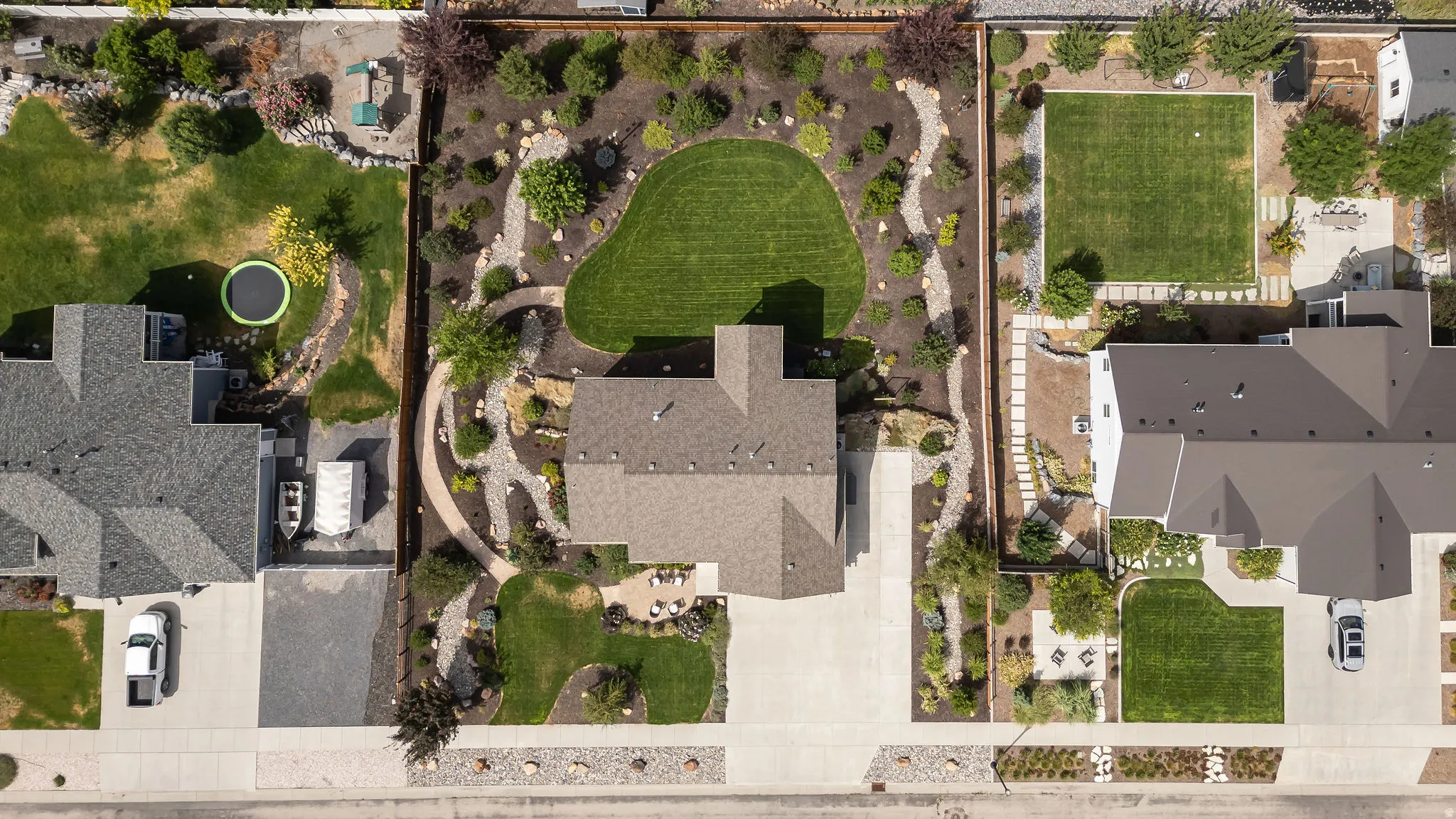 Expansive property featuring a meticulously landscaped backyard, concrete driveway, and established plantings