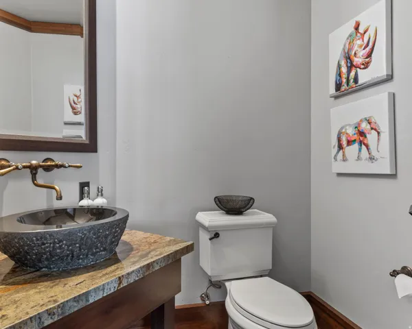 Floating vanity with a natural stone vessel sink, bronze-finish wall-mounted faucet, and wood-finish flooring