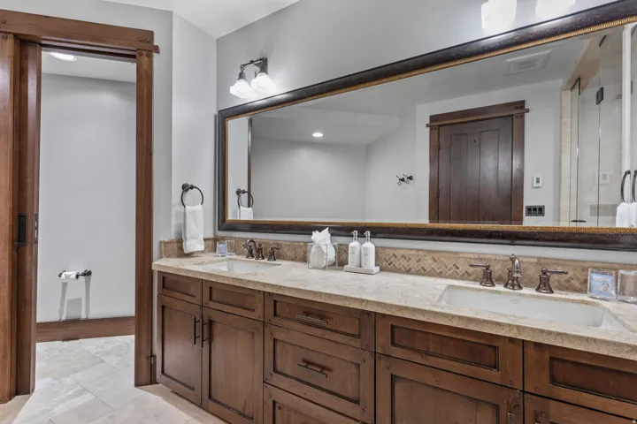Dual vanity with integrated sinks, stone countertop, wood-finish cabinetry, and a large framed mirror