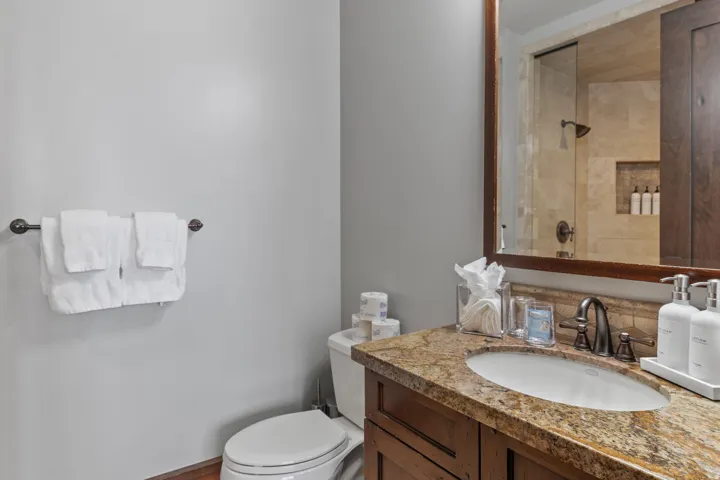 Vanity with a granite countertop and integral sink, wood-finish cabinetry, framed mirror, and a glass-enclosed shower with a tiled surround