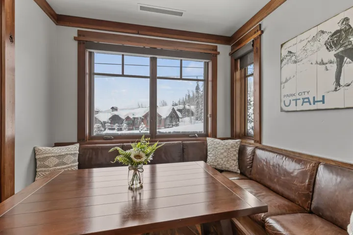 Built-in banquette seating with brown leather upholstery, a large wood-finish dining table, and wood-trimmed windows