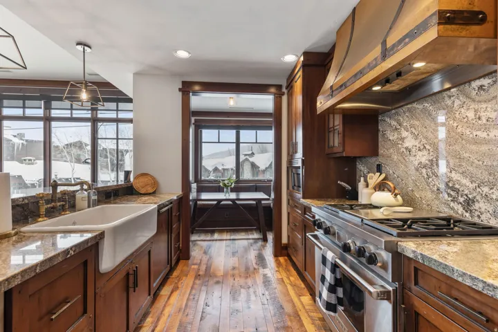 Gourmet kitchen with wood-finish flooring, custom wood cabinetry, stone countertops, a large farmhouse sink, and a commercial-grade gas range with a custom wood hood