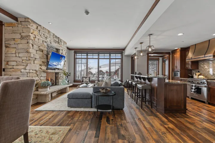 Stone-faced fireplace, large-pane windows, wood-finish flooring, breakfast bar with pendant lighting, and stainless steel range with custom hood