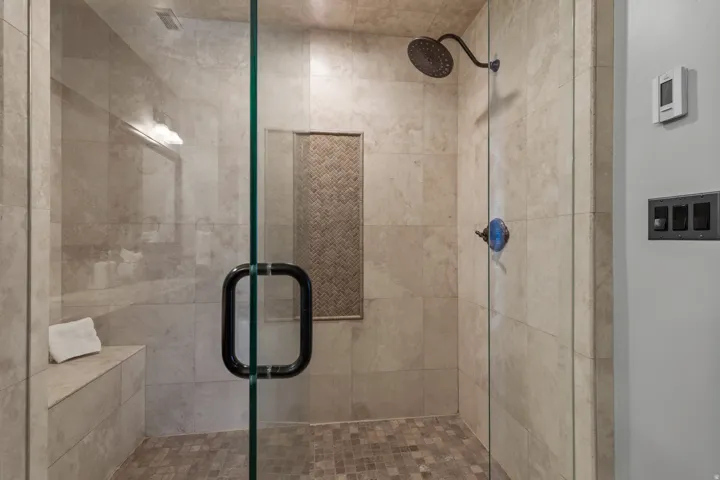 Glass-enclosed shower featuring large format wall tile, built-in bench, mosaic floor tile, and rain showerhead