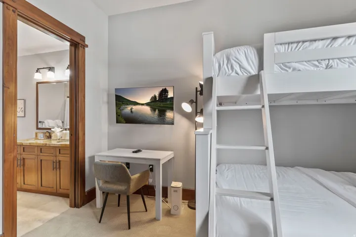 White bunk beds, wall-mounted television, and wood-trimmed doorway