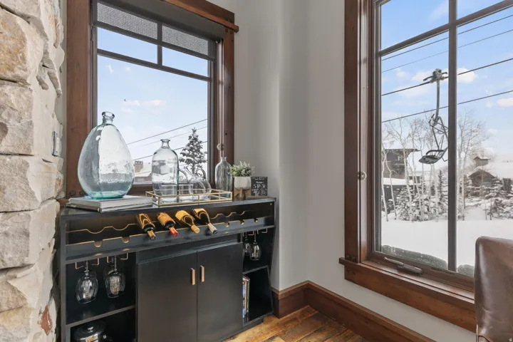 Built-in bar cabinet with wine storage, natural stone accent wall, and wood-framed windows