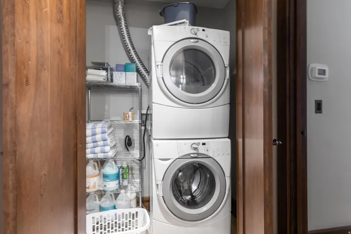Stacked laundry appliances within a closet, complemented by wood-finish doors and a metal shelving unit