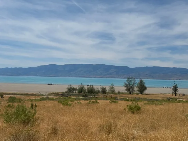 Expansive natural landscape featuring a body of water, distant mountains, and varied vegetation