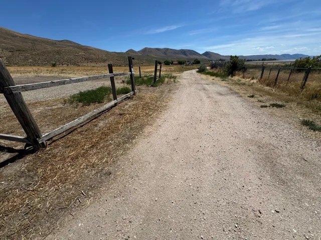 Gravel driveway bordered by a wooden fence, with distant mountains and a body of water under a clear sky