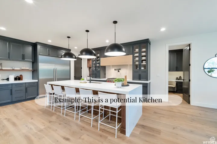 Spacious kitchen featuring an expansive center island, dark cabinetry, stainless steel refrigerator, contemporary pendant lighting, and wood-finish flooring