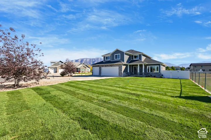 Expansive front lawn with striped landscaping, mature trees, and a two-story residence featuring a stone and siding exterior