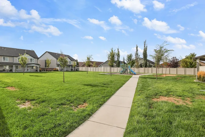 Expansive green space featuring a concrete pathway, perimeter fencing, and a playground structure