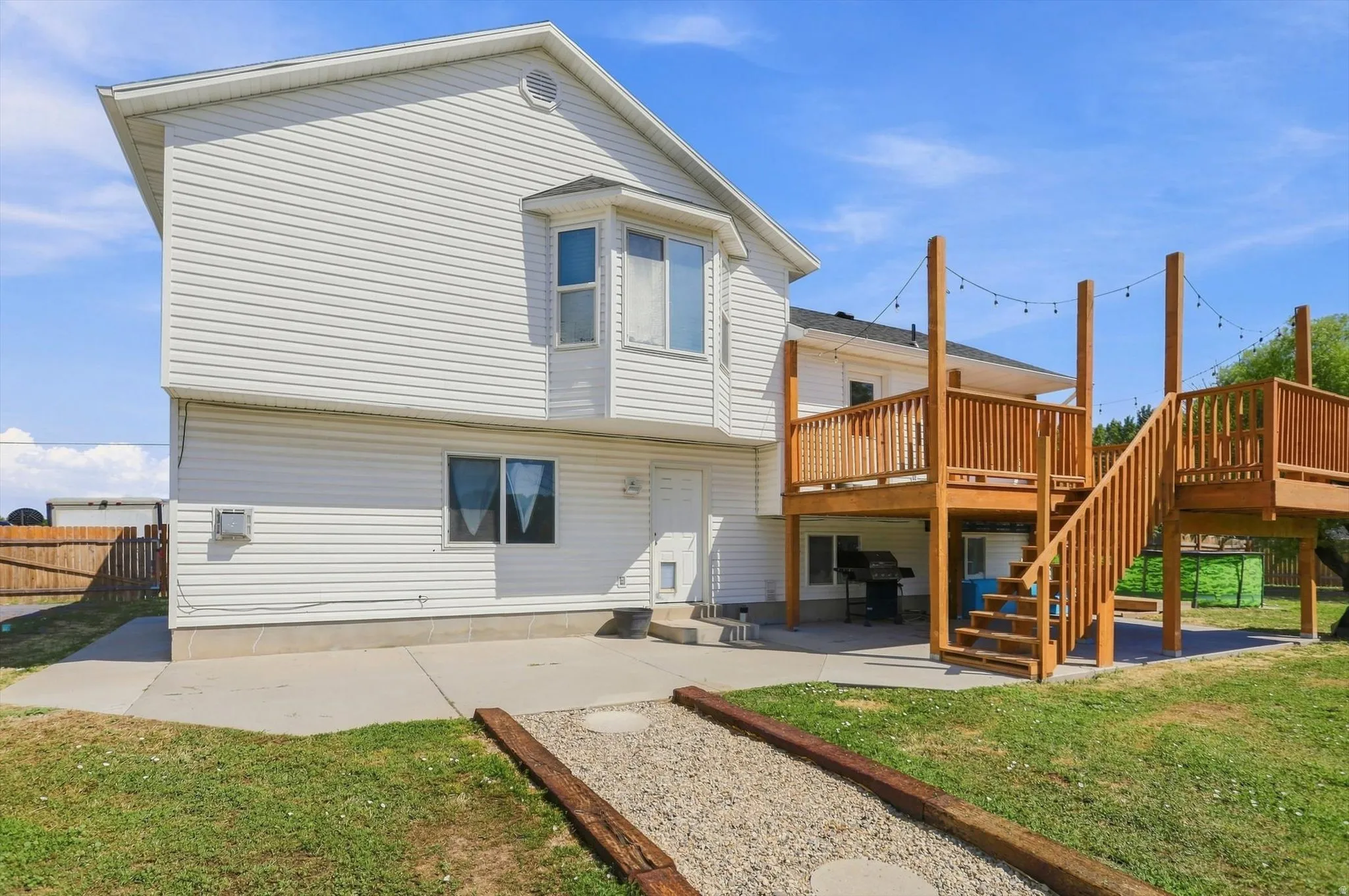 Multi-level wood deck with stairs, featuring a ground-level concrete patio and a bay window on the white siding exterior