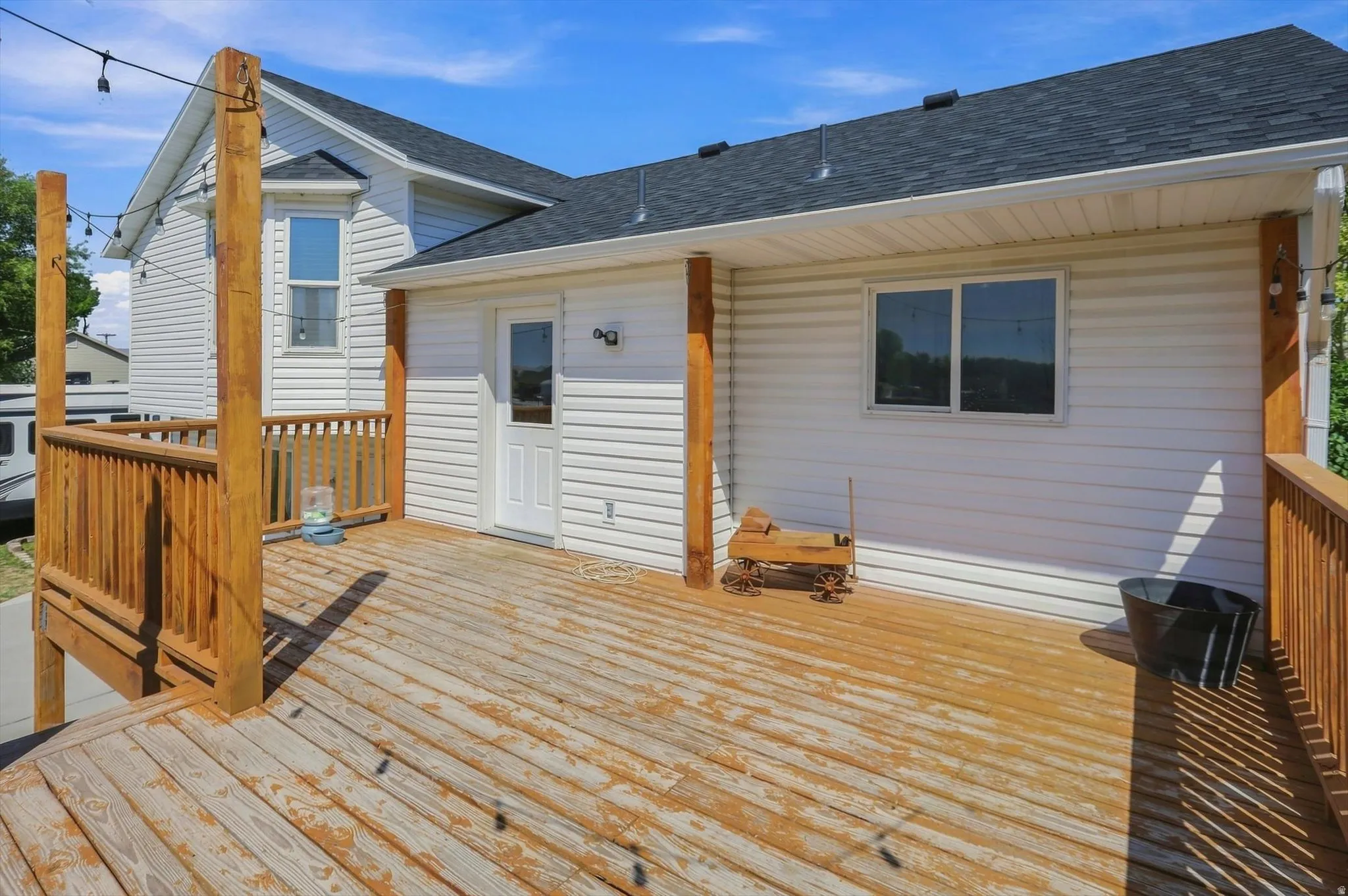 Expansive wood deck with wood railings, white siding exterior, dark shingle roof, and exterior door access