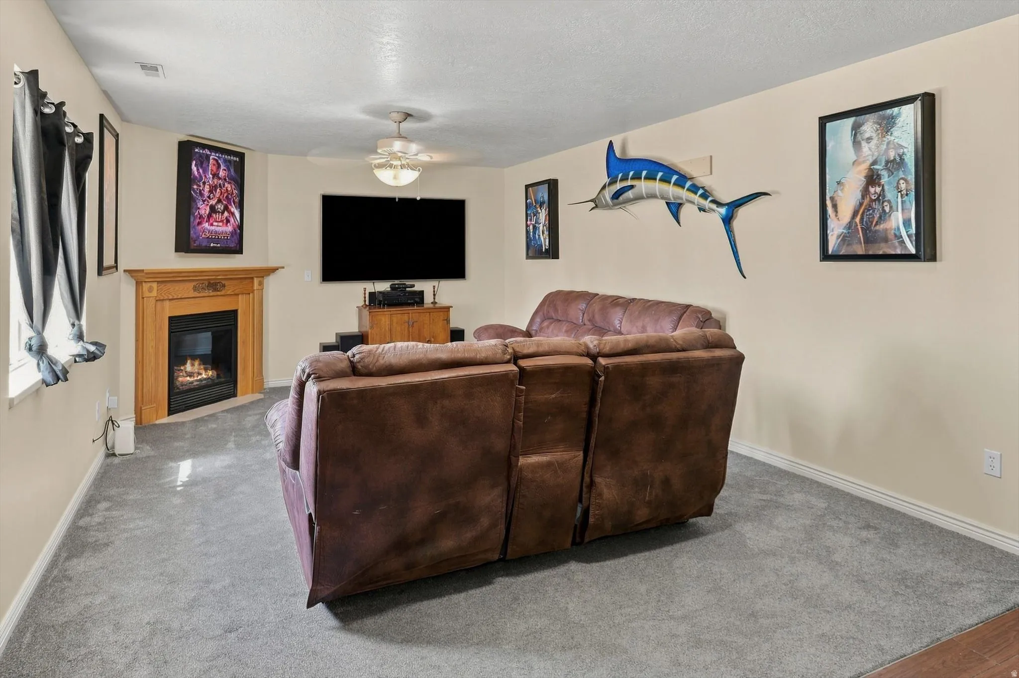 Carpeted room with a corner fireplace featuring a wood-finish mantel and a ceiling fan with integrated lighting