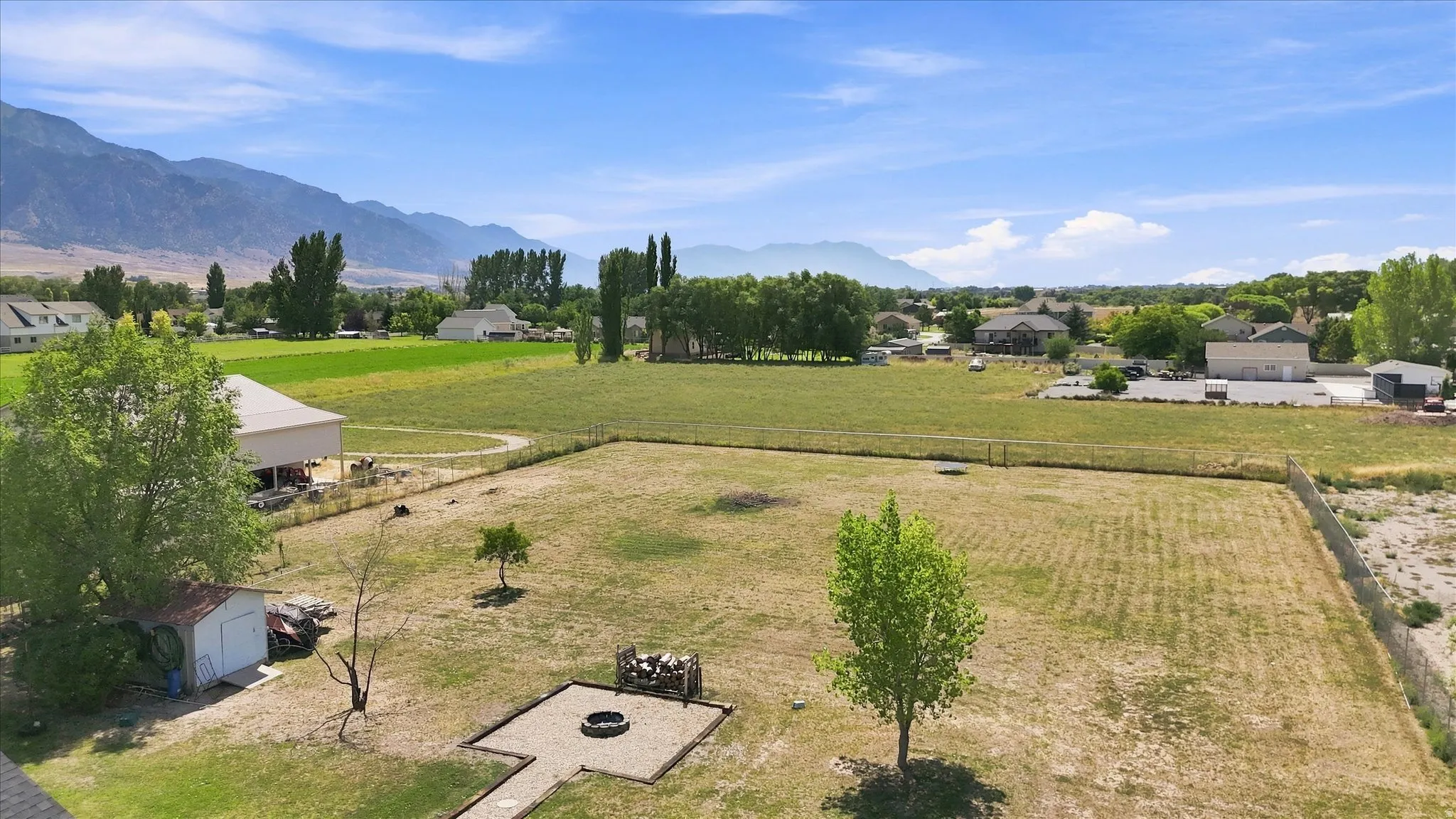 Expansive outdoor area featuring a fire pit with surrounding gravel, a white storage shed, and a large open field