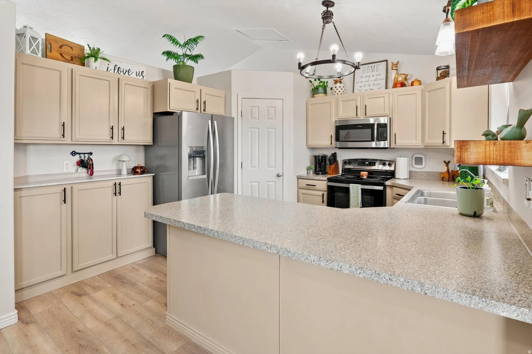 Kitchen featuring light-toned cabinetry, light-colored countertops, stainless steel appliances, a center island, and wood-finish flooring