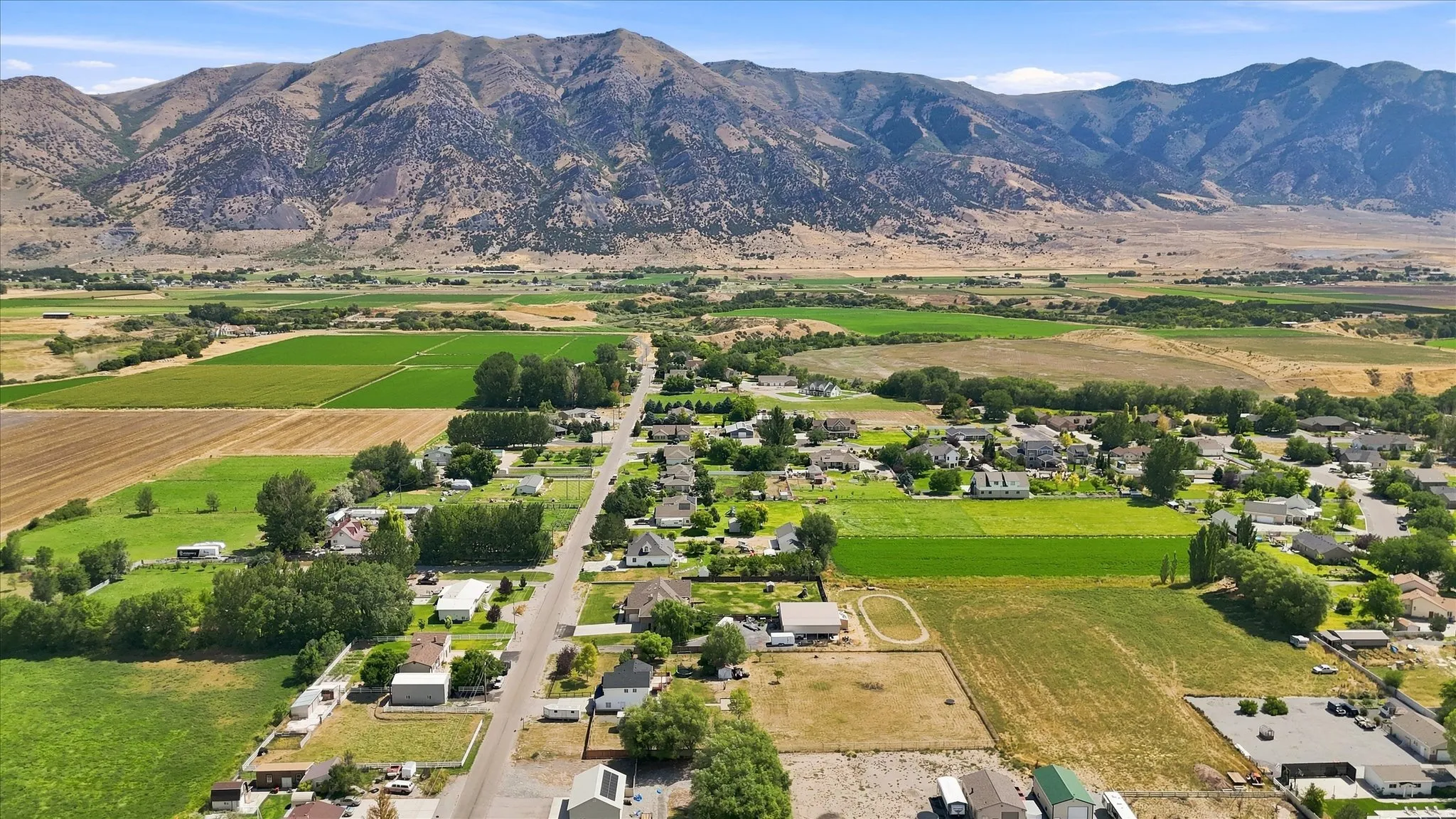 Mountain backdrop, expansive valley, scattered residential properties, agricultural fields, established road network