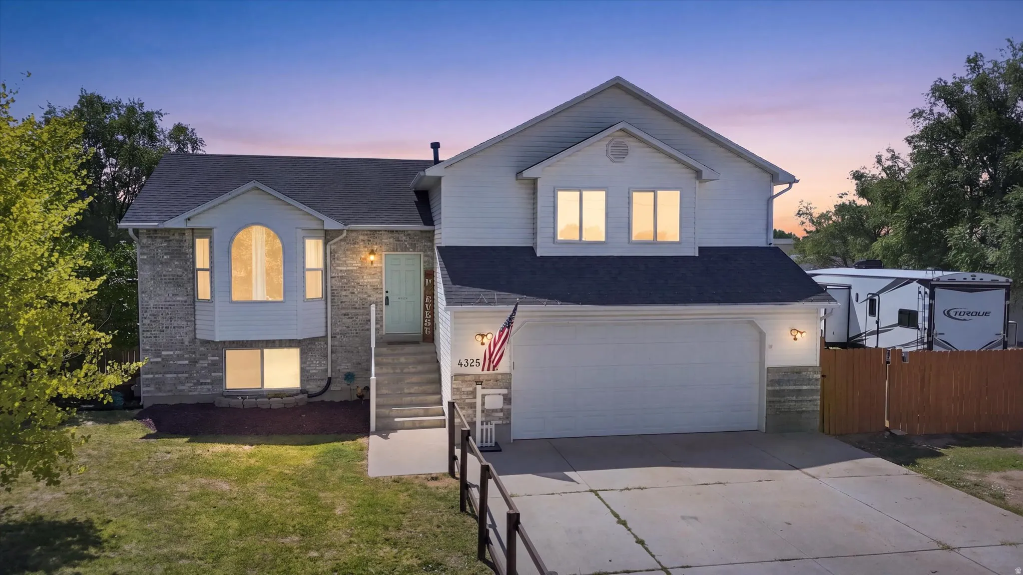 Split-level residence featuring a two-car garage, stone and siding exterior, arched window, and a light blue front door