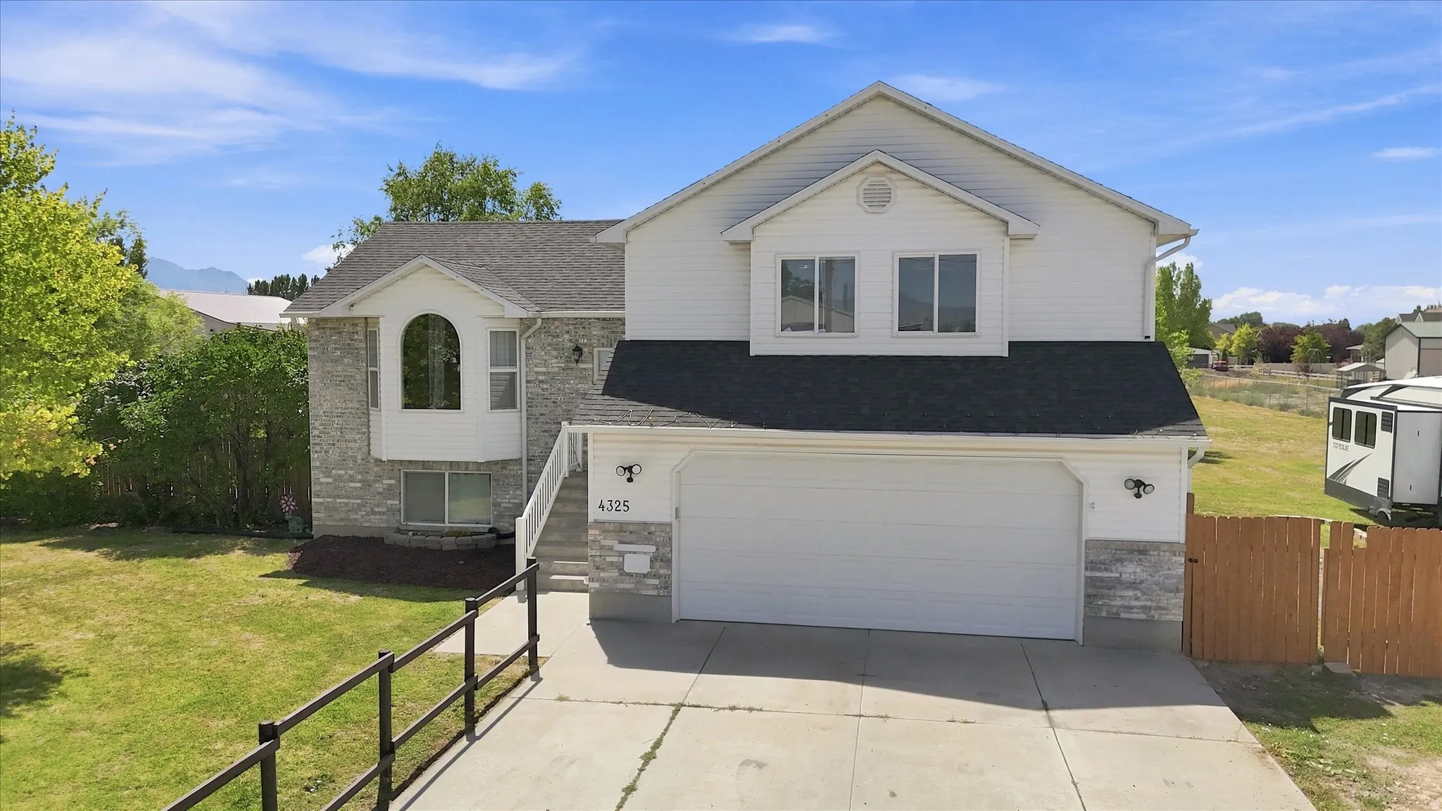 Multi-level residence featuring a stone and siding exterior, a two-car garage, and a manicured front lawn