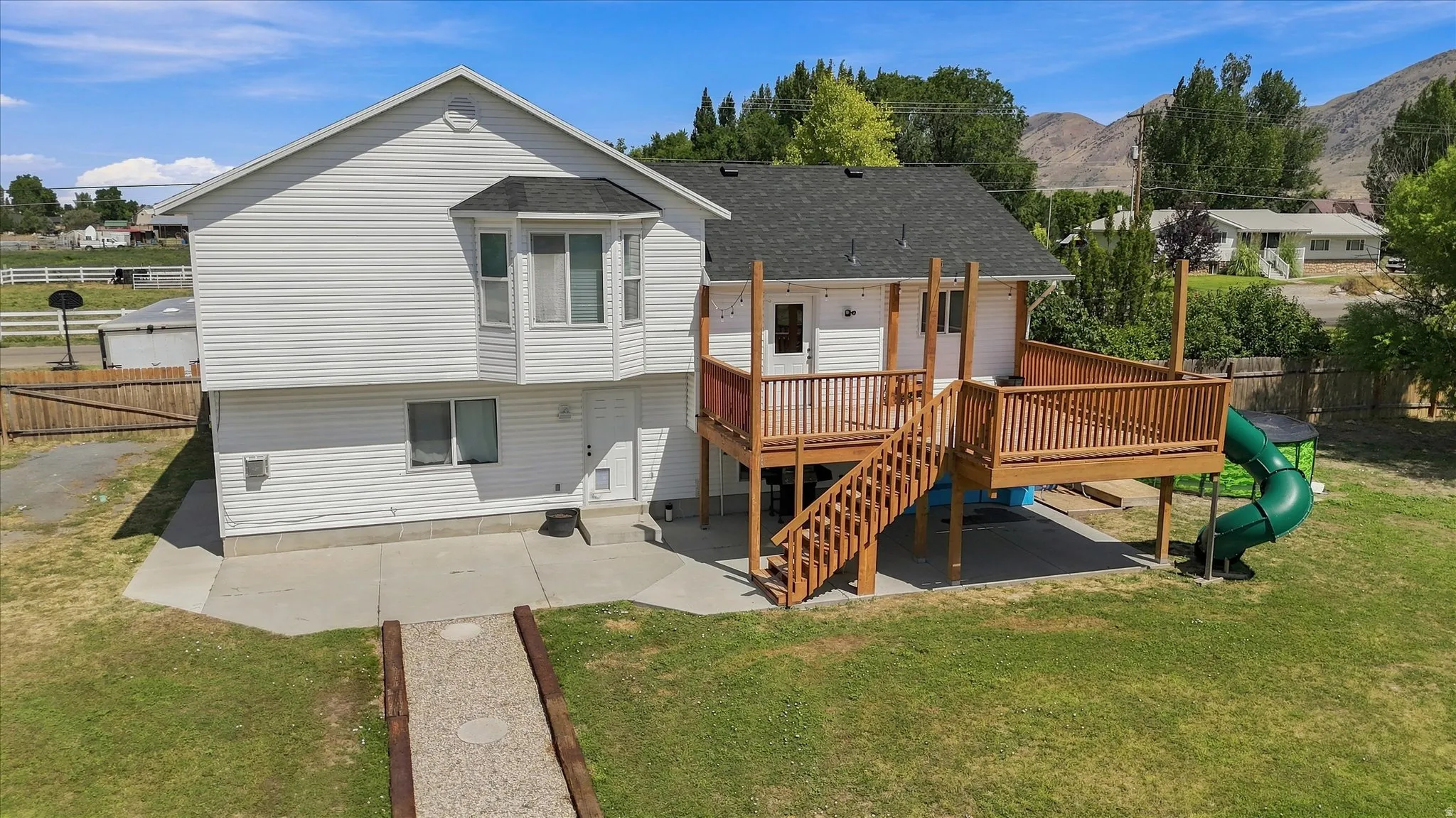 White siding exterior with a bay window, wood deck, and concrete patio
