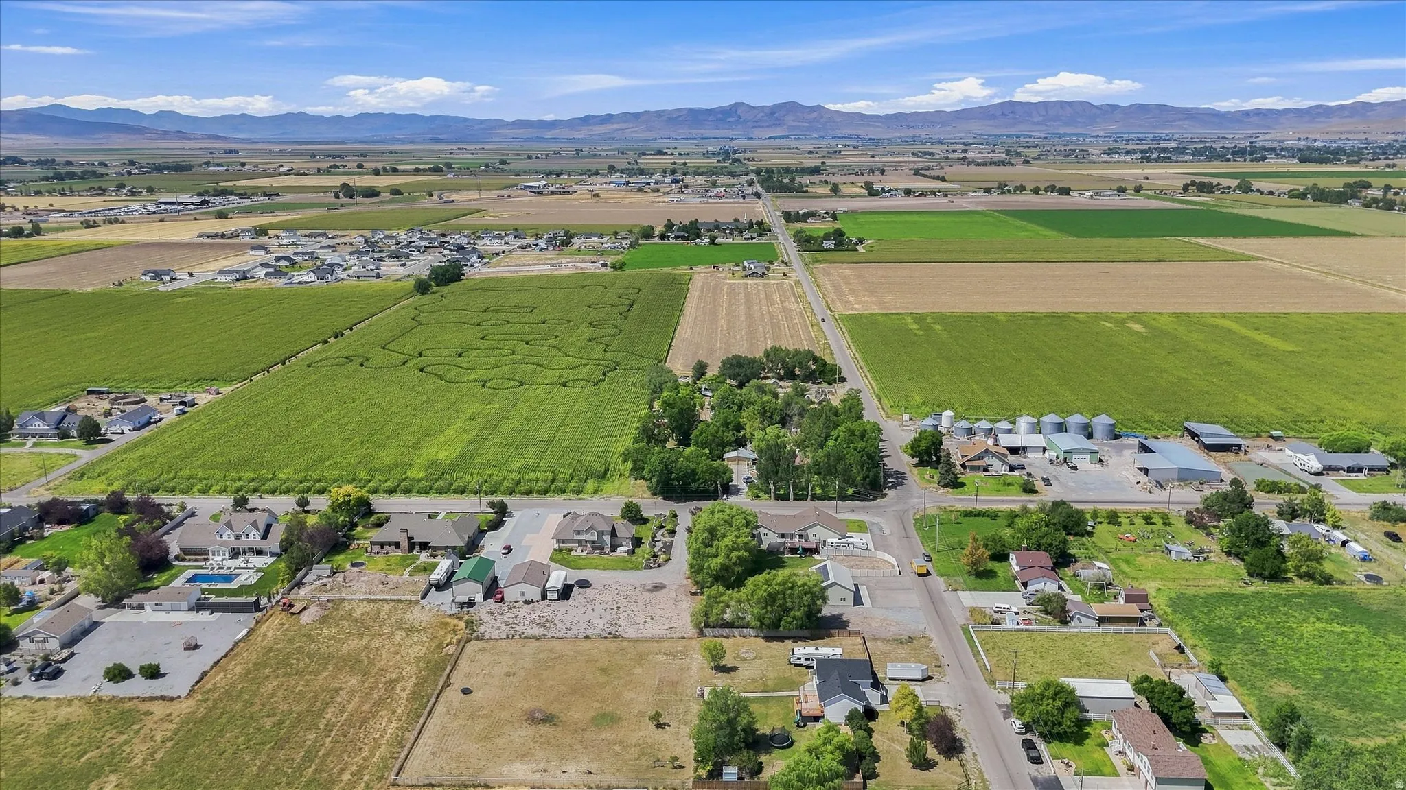 Expansive rural setting with mountain backdrop, agricultural fields, residential properties, and paved roads