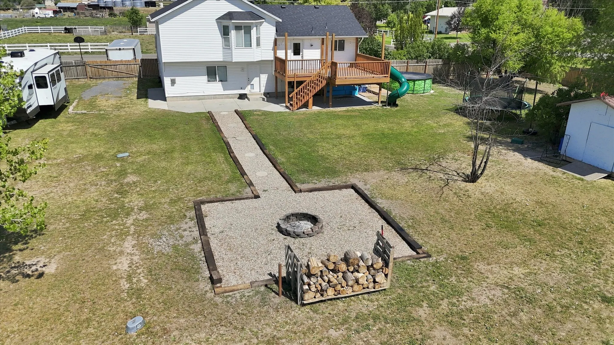 Expansive backyard featuring a gravel fire pit area with timber edging, a wood deck with stairs, and a concrete patio