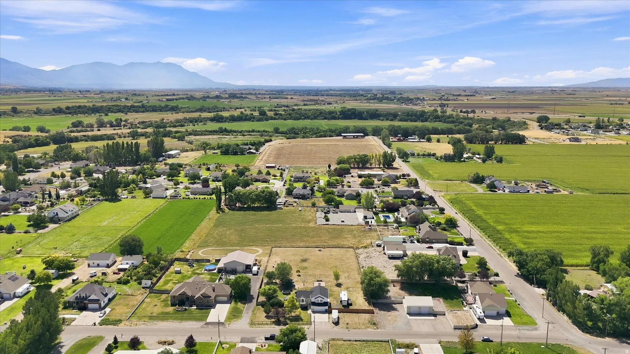 Expansive rural setting with a mountainous backdrop, visible residential structures, and agricultural fields