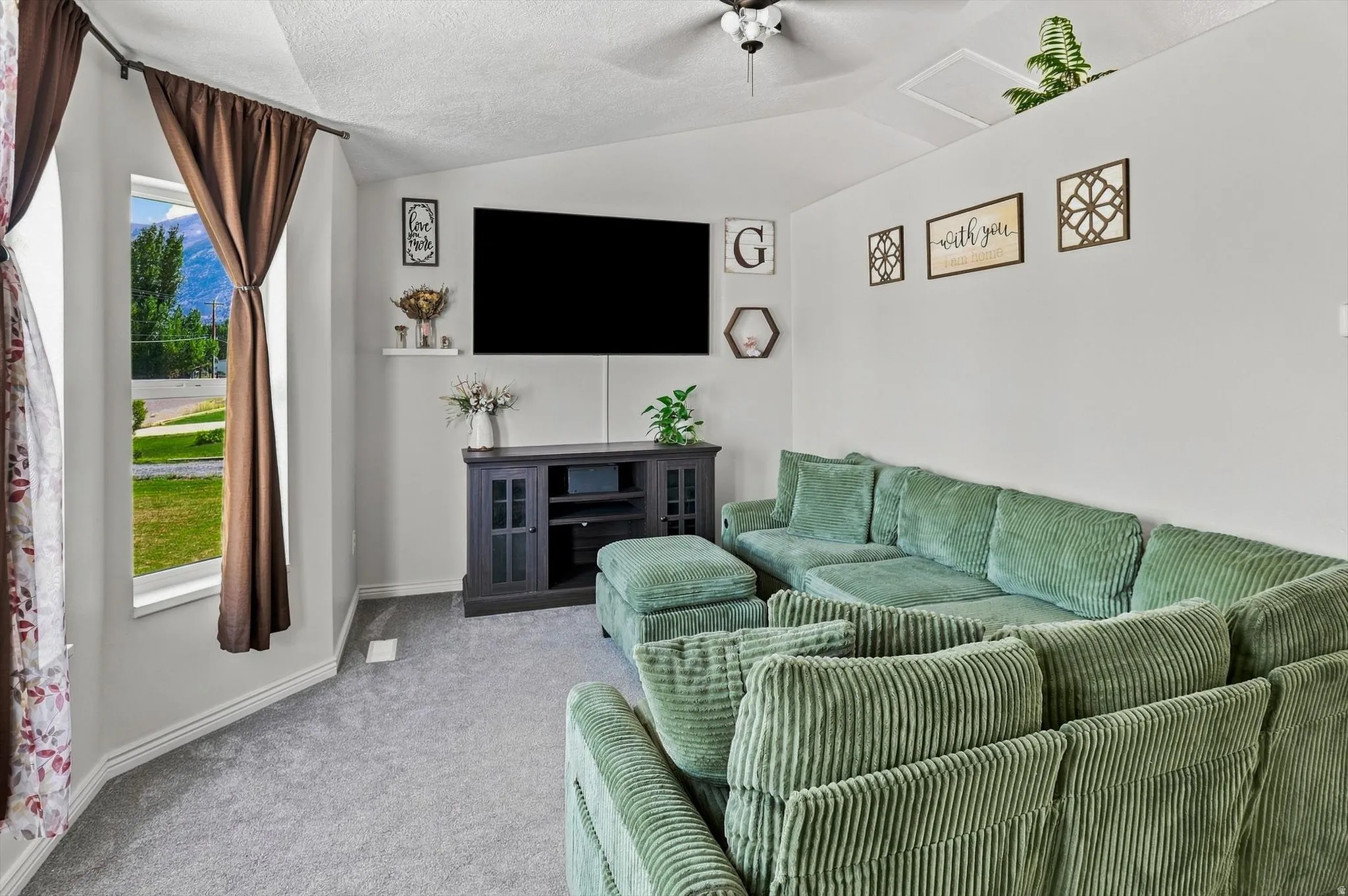 Vaulted ceiling with a ceiling fan, bay window with exterior mountain scenery, media console, and built-in wall ledge