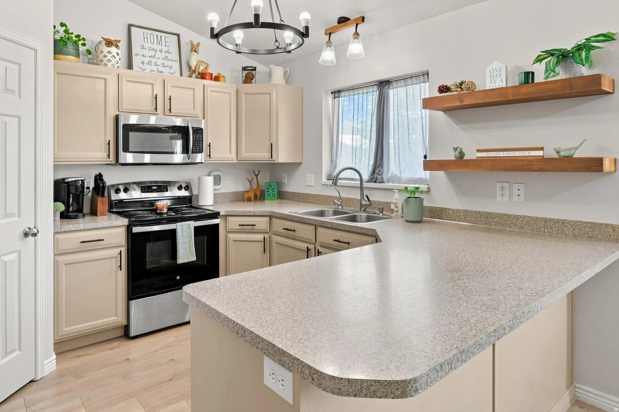 Kitchen featuring a double basin sink, stainless steel microwave, black-and-stainless steel range, wood-finish floating shelves, and light-toned cabinetry