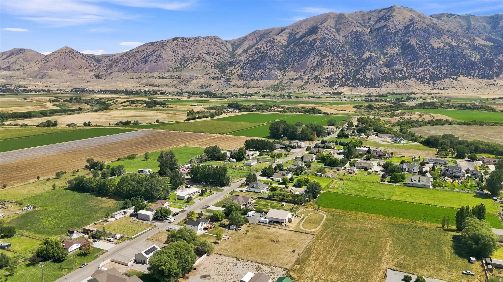 Expansive valley setting featuring a rural community, scattered homes, agricultural fields, and a prominent mountain range backdrop