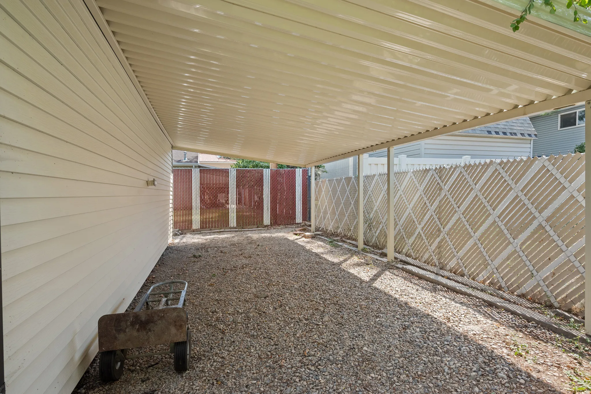 Covered exterior area featuring a corrugated metal roof, gravel ground cover, and a lattice fence